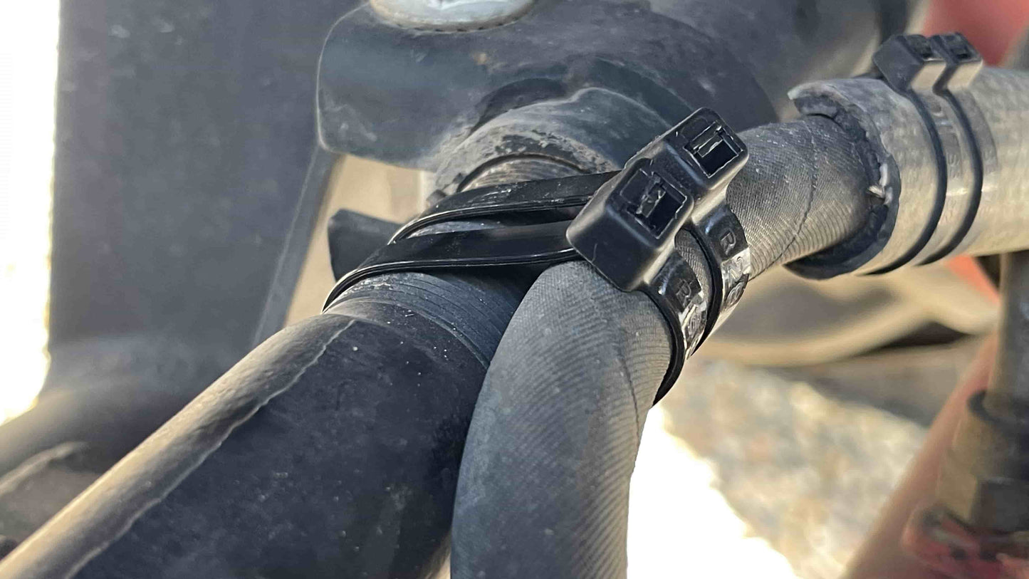 12-inch black industrial zip ties securing water pipes in an outdoor setting.