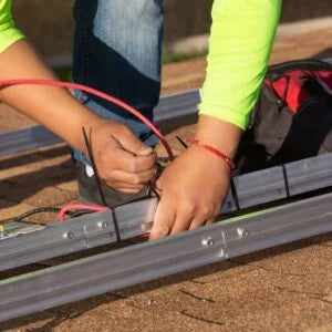 Hands securing a red wire to a metal frame using black zip ties, demonstrating the use of 24-inch, 175lb high-quality cable ties for electrical installations.