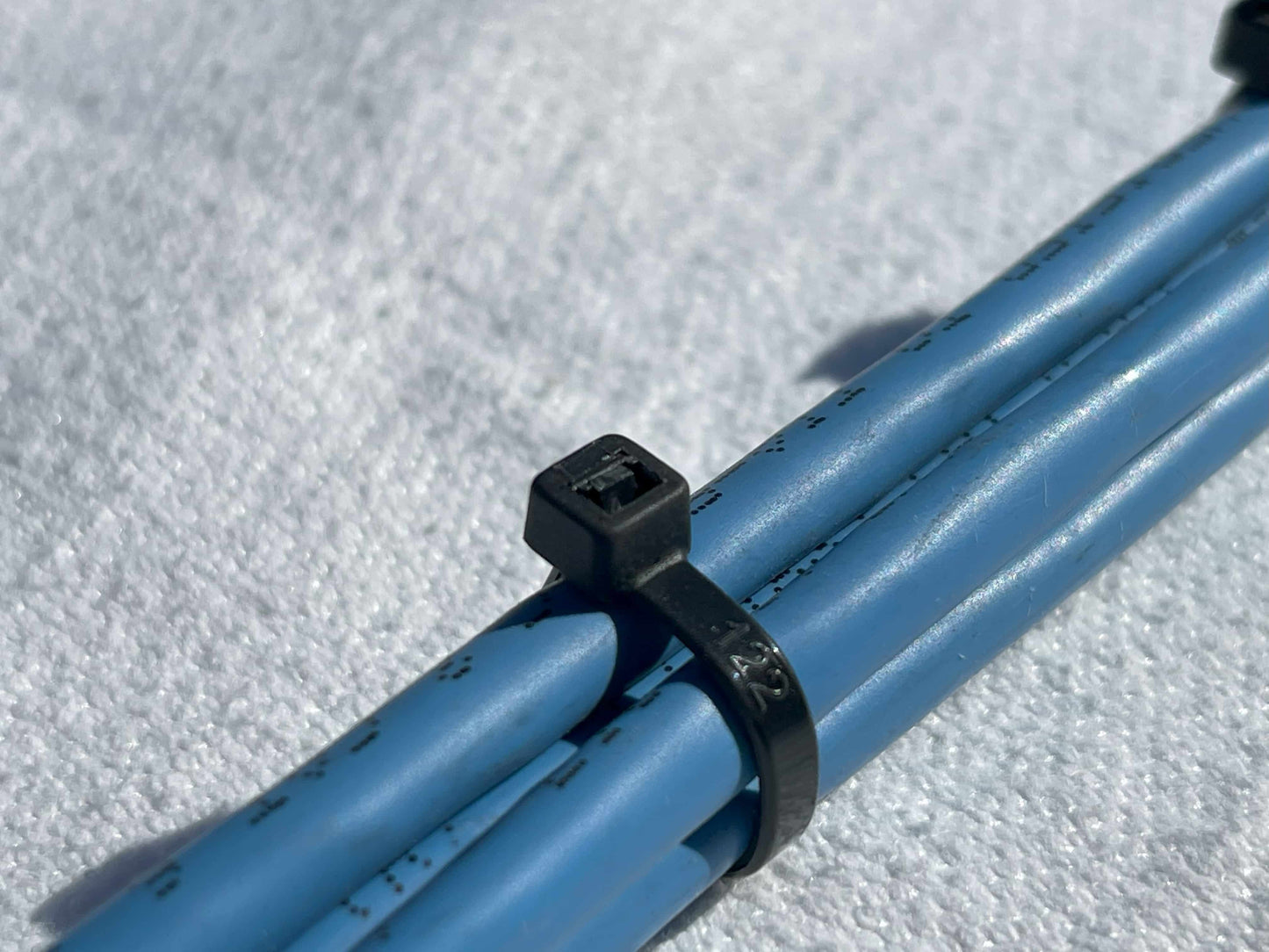 Close-up of a 4-inch black zip tie securing blue cables, highlighting cable management capabilities.